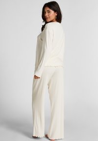 Cremekleurige geribde lounge-outfit met lange mouwen en wijde broekspijpen. Kenmerkt zich door golvende randen en een ontspannen pasvorm voor comfort.