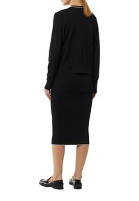 Schwarzes gestreiftes Sweater- und Rockset mit einem verkürzten Design, langen Ärmeln und weißem Saum, kombiniert mit glänzenden schwarzen Schuhen.