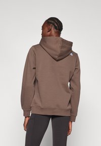 Sweatshirt marrom com capuz, com punhos e barra canelados, apresentando um pequeno logótipo na parte superior das costas. O material parece suave e texturizado.