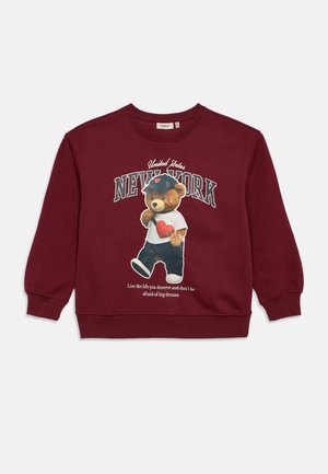 Bordó pulóver macival, sapkában és szívmintás ingben, "United States NEW YORK" felirattal, és motivációs idézettel alul.