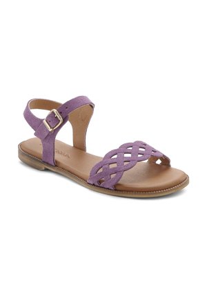 Purple suede sandal with crisscross strap design, flat brown leather sole, adjustable ankle strap, and metallic buckle detail.