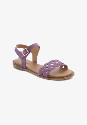 Purple suede sandal with crisscross strap design, flat brown leather sole, adjustable ankle strap, and metallic buckle detail.