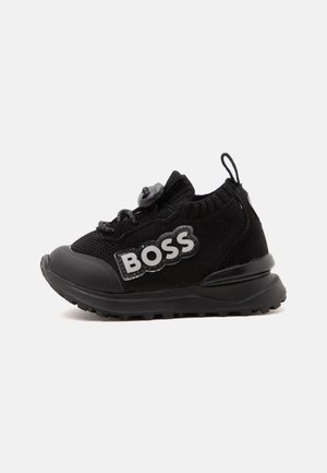Schwarzer Kleinkind-Sneaker mit gestricktem Obermaterial, dicker Sohle, Zuglasche an der Ferse und "BOSS"-Logo an der Seite in weißen Buchstaben.