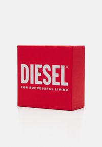 Rdeča škatla z velikimi belimi črkami "DIESEL", zgornja stran prikazuje slogan "ZA USPEŠNO ŽIVLJENJE." Gladka tekstura, kvadratna oblika.
