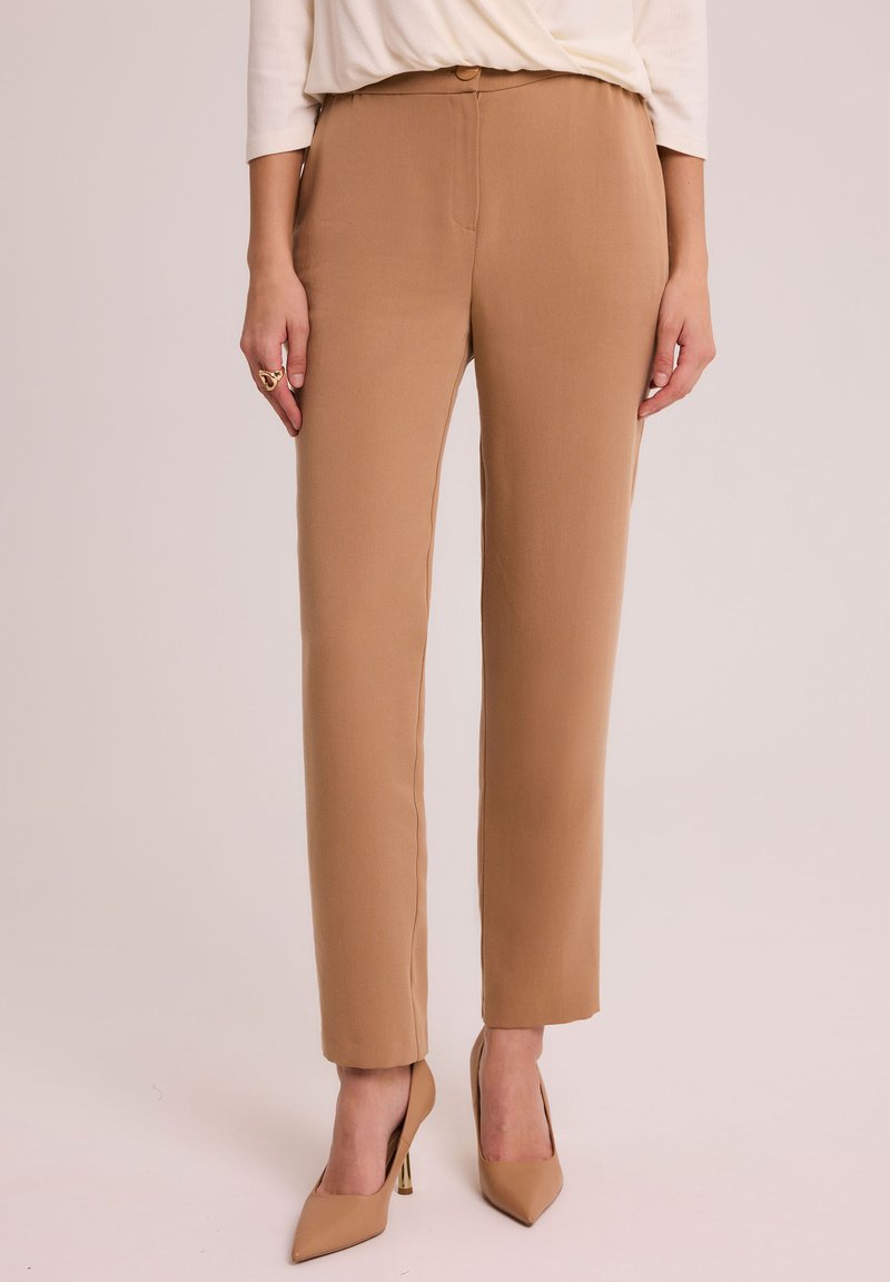 Spodnie w kolorze taupe o gładkiej fakturze, zwężanym kroju i z przodu zapinane na guzik. Połączone z beżowymi szpilkami.