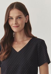 Navy V-neck top with short sleeves, featuring a textured fabric and small, evenly spaced gold dots throughout.