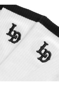 Fehér bordázott zoknik fekete szegéllyel. A elején fekete hímzett "bd" inicialék találhatók. Puha tapintású és közepes hosszúságú.