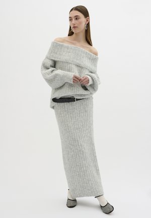 Grey ribbed knit off-shoulder sweater paired with a matching long skirt and a black belt. Accented with textured footwear featuring a pattern.