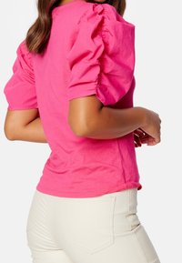 Top de algodón rosa ajustado con mangas abullonadas, escote redondo y una textura suave. Combinado con pantalones ajustados de color claro.