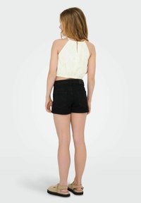 Zwarte spijkershorts met een hoge taille, gecombineerd met een witte kanten crop top met een keyhole rug. Schoenen zijn beige met een stevige zool.