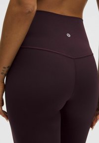 Legíny s vysokým pasem v tmavě burgundské tkanině. Mají bezešvou konstrukci, hladkou texturu a logem na pase.