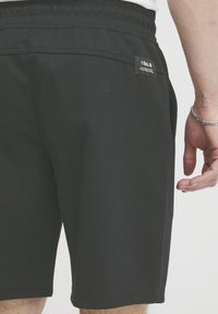 Shorts de sport noirs en tissu texturé, dotés d'une poche arrière et d'une étiquette !SOLID sur la taille. Design simple et à coupe droite.