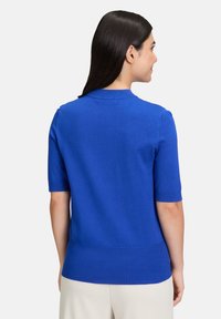 Maglione azzurro a maniche corte in maglia con collo rotondo e orlo a coste. Texture liscia e silhouette aderente senza ulteriori decorazioni.