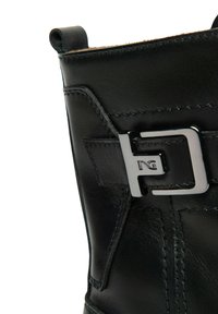 Stivale in pelle nera con una trama liscia, caratterizzato da un accento in metallo con fibbia e dettagli di cucitura a contrasto lungo il lato.