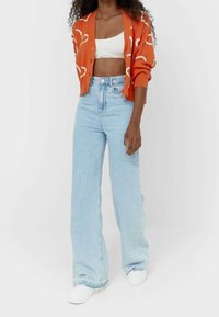 Orange kavaj med vita abstrakta mönster, i kombination med ljusblå vida jeans. En vit croppad topp och vita sneakers fulländar outfiten.