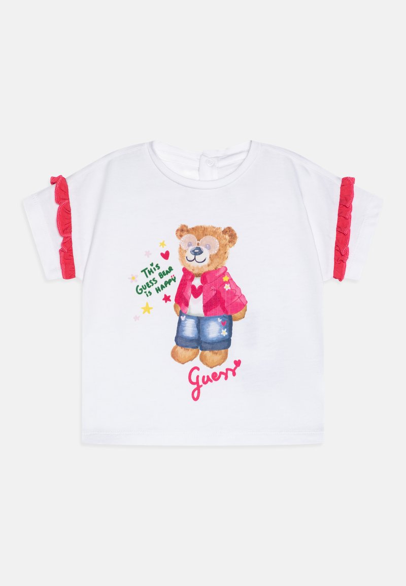 Vit kortärmad t-shirt med en björn i röd jacka och denimshorts med rosa volanger på ärmarna. "Guess"-logotyp i rosa text.