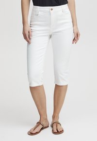 Bílé capri kalhoty vyrobené z elastického denimu, s polovičním pasem, pěti kapsami a jedním knoflíkem na zapínání. Hladký povrch s mírným leskem.