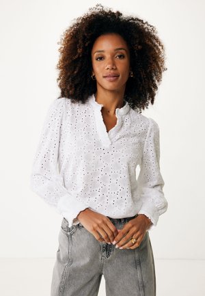 Chemisier blanc à manches longues avec motif broderie anglaise et col volanté. Dispose de manches bouffantes avec poignets élastiques et d'une coupe décontractée.
