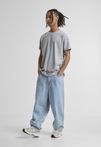 Tricou din bumbac gri cu o croială lejeră, asortat cu blugi largi de culoare albastru deschis și adidași în nuanțe neutre. Design minimalist, textură fină.