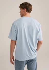 Hellblaues Baumwoll-T-Shirt mit lockerem Schnitt und kurzen Ärmeln. Der Rücken hat ein einfaches Design ohne sichtbare Logos oder Muster.