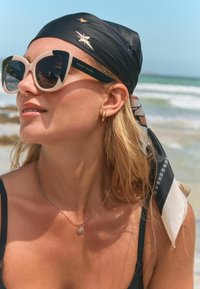 Mustad ja kreemilised prillid, millel on ülepaisutatud kassisilma disain. Must sall metallsete tähe aktsentidega. Kuldne rõngaskõrvarõngas ja päikesependeliga kaelakee.