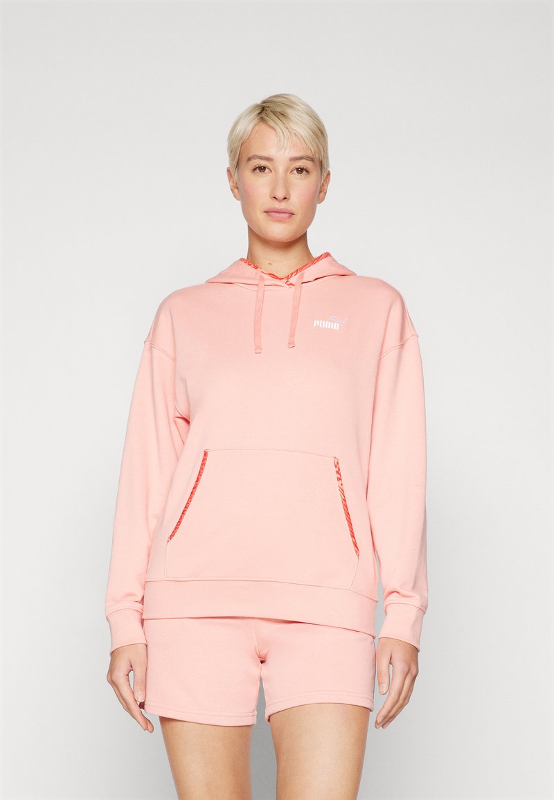 Rosa hettegensere med lommer foran og snorlukking. Korte rosa shorts. Begge er laget av mykt stoff og har en subtil logo på brystet.