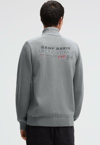 Grauer, strukturierter Pullover mit gerippten Bündchen und Saum. Rückseite mit der Aufschrift "CAMP DAVID ARCTIC VOYAGE" in fetten Buchstaben. Lässiges Design, lange Ärmel.