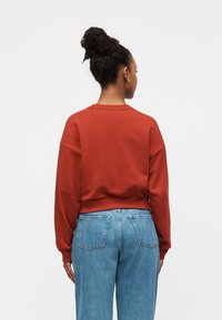 Φούτερ σε χρώμα σκουριάς με άνετη εφαρμογή, ριμπ μανσέτες και τελείωμα, σε συνδυασμό με ανοιχτόχρωμο τζιν ψηλόμεσο. Απλός σχεδιασμός, ελάχιστες λεπτομέρειες.