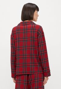 Czerwona koszula w kratę z klasycznym kołnierzykiem, długimi rękawami i luźnym krojem, z czarnymi i zielonymi akcentami w kratkowanym wzorze.