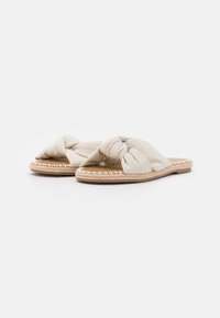 Beige schuifsandalen met een geknoopte stoffen bovenkant, geweven jute zool en platte bodem. Kenmerkend zijn de gladde textuur en het minimalistische ontwerp.