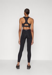 Svart atletisk antrekk med racerback sports-BH med utskjæringsdetalj og høytlivsleggings, begge laget av elastisk stoff.