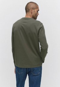 Långärmad, olivgrön t-shirt i bomull med rund halsringning och rak skärning, kombinerad med blå denimjeans.