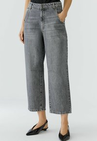 Graue Denim-Jeans mit weiter Beinform und hohem Bund, ausgestattet mit Fronttaschen, dezenten Nahtdetails und einem cropped Schnitt. Schwarze Slingback-Schuhe.