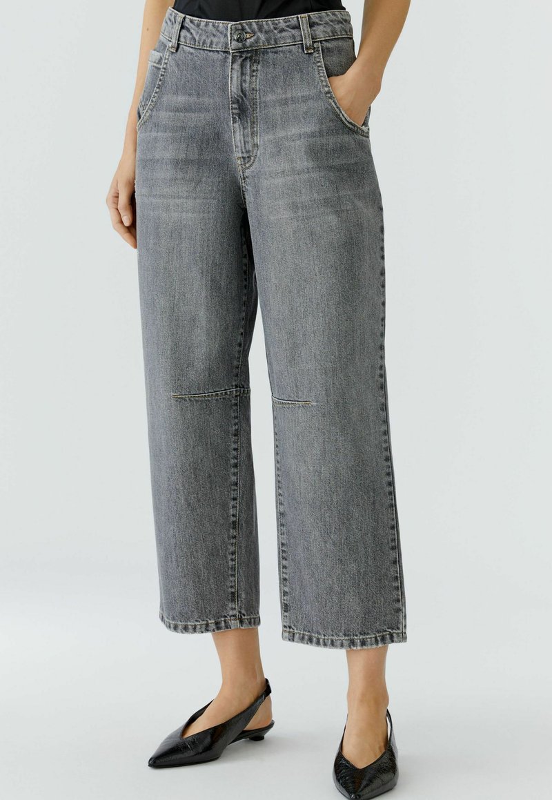 Graue Denim-Jeans mit weiter Beinform und hohem Bund, ausgestattet mit Fronttaschen, dezenten Nahtdetails und einem cropped Schnitt. Schwarze Slingback-Schuhe.