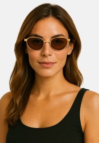Owalne okulary przeciwsłoneczne z cienką złotą ramką i brązowymi, przyciemnionymi soczewkami, na jasnym tle. Noszone przez osobę o długich, falowanych włosach.