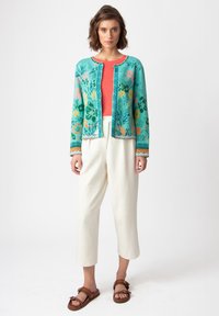 Cárdigan turquesa con estampados florales, blusa roja, pantalones de pierna ancha color crema y sandalias marrones con acentos multicolores.