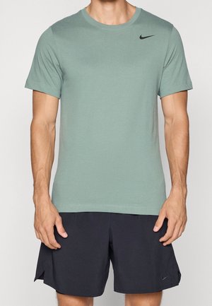 Man wearing sage green Nike short-sleeve crew neck t-shirt and black Nike athletic shorts, standing with hands relaxed by sides.