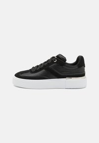 Black sneaker with a smooth leather upper, suede accents, flat laces, and a thick white platform sole with a textured tread.