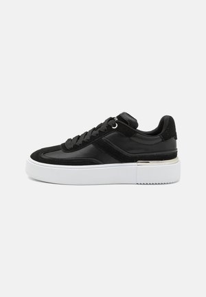 Black sneaker with a smooth leather upper, suede accents, flat laces, and a thick white platform sole with a textured tread.