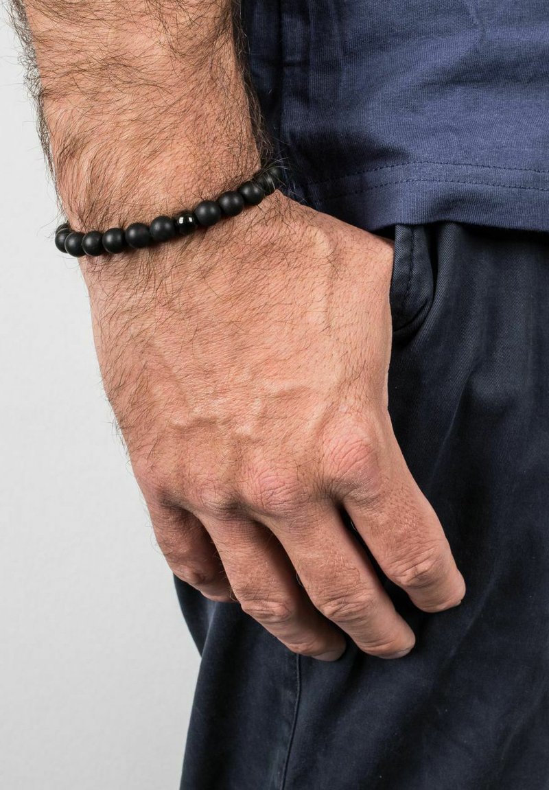 Black bead bracelet with smooth spherical beads, featuring a single glossy accent bead, worn on a hand against a dark shirt.