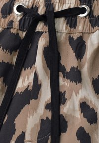 Lien noir passé à travers des œillets métalliques sur une ceinture en tissu imprimé animal beige et noir.