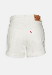 Pantalones cortos de mezclilla blanca con dobladillo enrollado, dos bolsillos traseros y una etiqueta de cuero marrón. Presentan costuras rojas en el bolsillo.