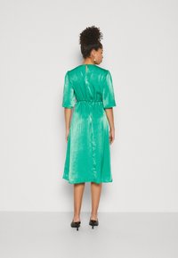 Schimmerndes grünes Midikleid mit kurzen Ärmeln, tailliertem Bund und Rückenausschnitt. Glatte Textur, fließende Form und Knielänge.