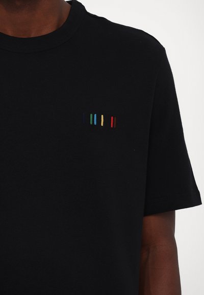 T-shirt en coton noir à col rond, avec une broderie verticale multicolore sur la poitrine gauche, incluant du bleu, du vert, du jaune et du rouge.