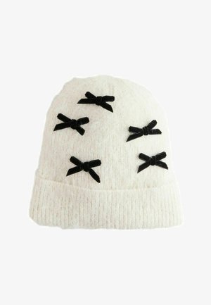 Hvid strikket beanie-hat pyntet med fem små sorte fløjlsbuer spredt ud over fronten.