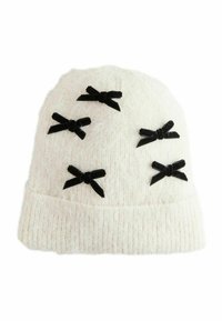 Bonnet tricoté blanc orné de six nœuds en velours noir. Le tissu texturé avec un revers à la base ajoute du détail au design.