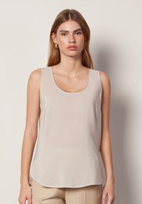 Beige ärmlös topp med rundad halsringning, mjuk textur och rundad nederkant. Tyget verkar lätt och något glansigt.