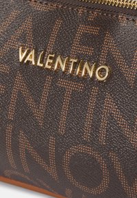 Rjava usnjena torba z zlato "VALENTINO" logo in diskretnim oranžnim vzorcem. Ima zadrgo in gladek rob.