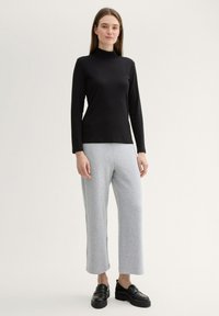 Suéter negro de manga larga con cuello de tortuga, textura acanalada, combinado con pantalones de chándal grises de pierna ancha. El calzado son mocasines negros con suela gruesa.