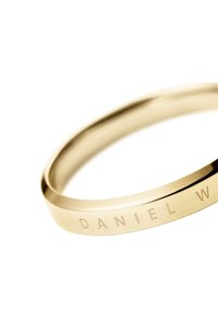 Bracciale in metallo dorato con una superficie liscia e lucida e un'incisione "DANIEL W" sulla fascia esterna, caratterizzato da un design rotondo.